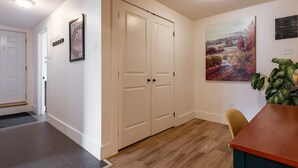 A hallway with a wooden floor, white walls, a white door, a coat rack, and a painting.