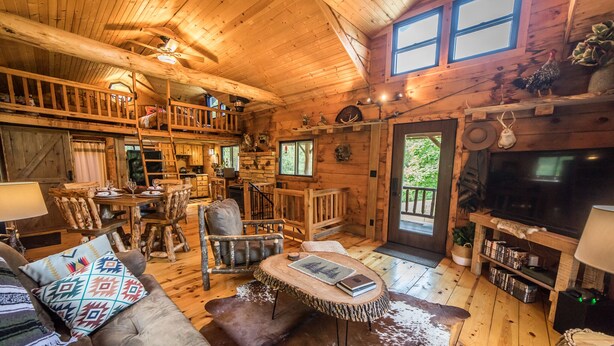 A rustic cabin interior with a dining area, a cozy seating area with a fireplace, and a television.