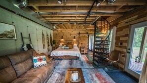 A cozy cabin interior with a wooden ceiling, a bed with a striped blanket, a brown leather sofa, and a small table with candles.