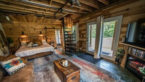 A cozy log cabin interior with a bed, sofa, wooden chest, and a fireplace.