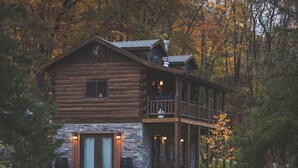 A log cabin with a stone foundation, a balcony, and a stone fireplace.