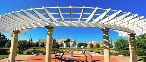 Un pavillon abrité, doté d’un sol en briques et de bancs, entouré de verdure et bordé par un plan d’eau.