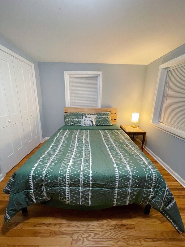 Un dormitorio con cama, mesita de noche, ventana con persianas y puerta.