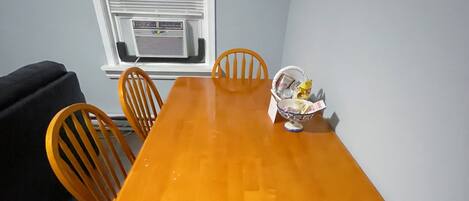 Un coin repas avec une table en bois et quatre chaises. Un panier contenant divers objets est posé sur la table.