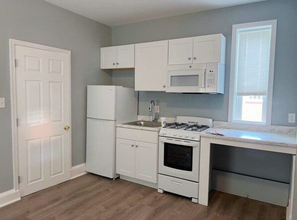 A compact kitchen with white cabinets, a refrigerator, a microwave, a stove, and a window with blinds. - Entire place with private parking (Wilmington)