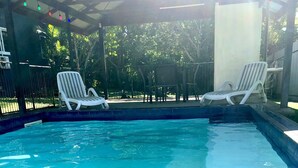 A swimming pool with tiled edges, surrounded by grass and white lounge chairs. - Cheerful Bungalow with pool! (Apia)