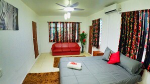 A bedroom with a bed, a red sofa, a ceiling fan, and curtains. - Cheerful Bungalow with pool! (Apia)
