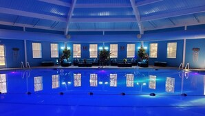 An indoor swimming pool with blue walls and ceiling, surrounded by seating areas and potted plants.
