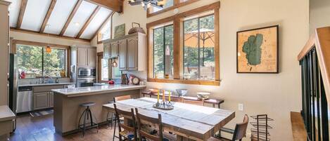 A spacious kitchen with wooden beams, large windows, and a dining area with a wooden table and chairs.