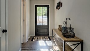 A hallway with a dark door, a wooden bench with a basket, and a striped rug. - 5 Star Cabin | Pet Friendly | Rushing Creek | Mountain Views | Foosball |Firepit (Cleveland)