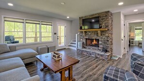 A living room with a stone fireplace, a sofa, a coffee table, and a television mounted above the fireplace. - 5 Star Cabin | Pet Friendly | Rushing Creek | Mountain Views | Foosball |Firepit (Cleveland)