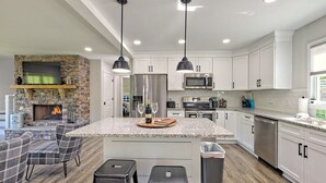 A modern kitchen with white cabinets, a stone fireplace, and a central island with bar stools. - 5 Star Cabin | Pet Friendly | Rushing Creek | Mountain Views | Foosball |Firepit (Cleveland)