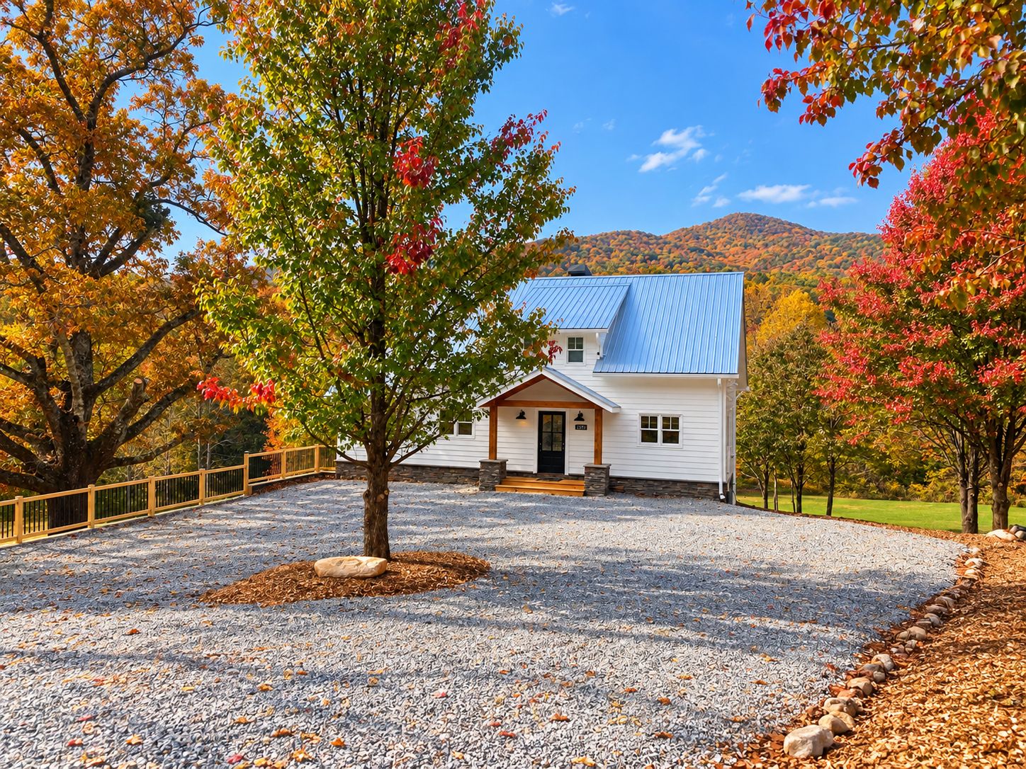 A house with a gravel driveway, surrounded by trees with autumn foliage.