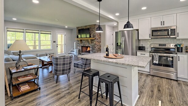 A spacious kitchen with modern appliances, a stone fireplace, and a large island with bar stools. - 5 Star Cabin | Pet Friendly | Rushing Creek | Mountain Views | Foosball |Firepit (Cleveland)