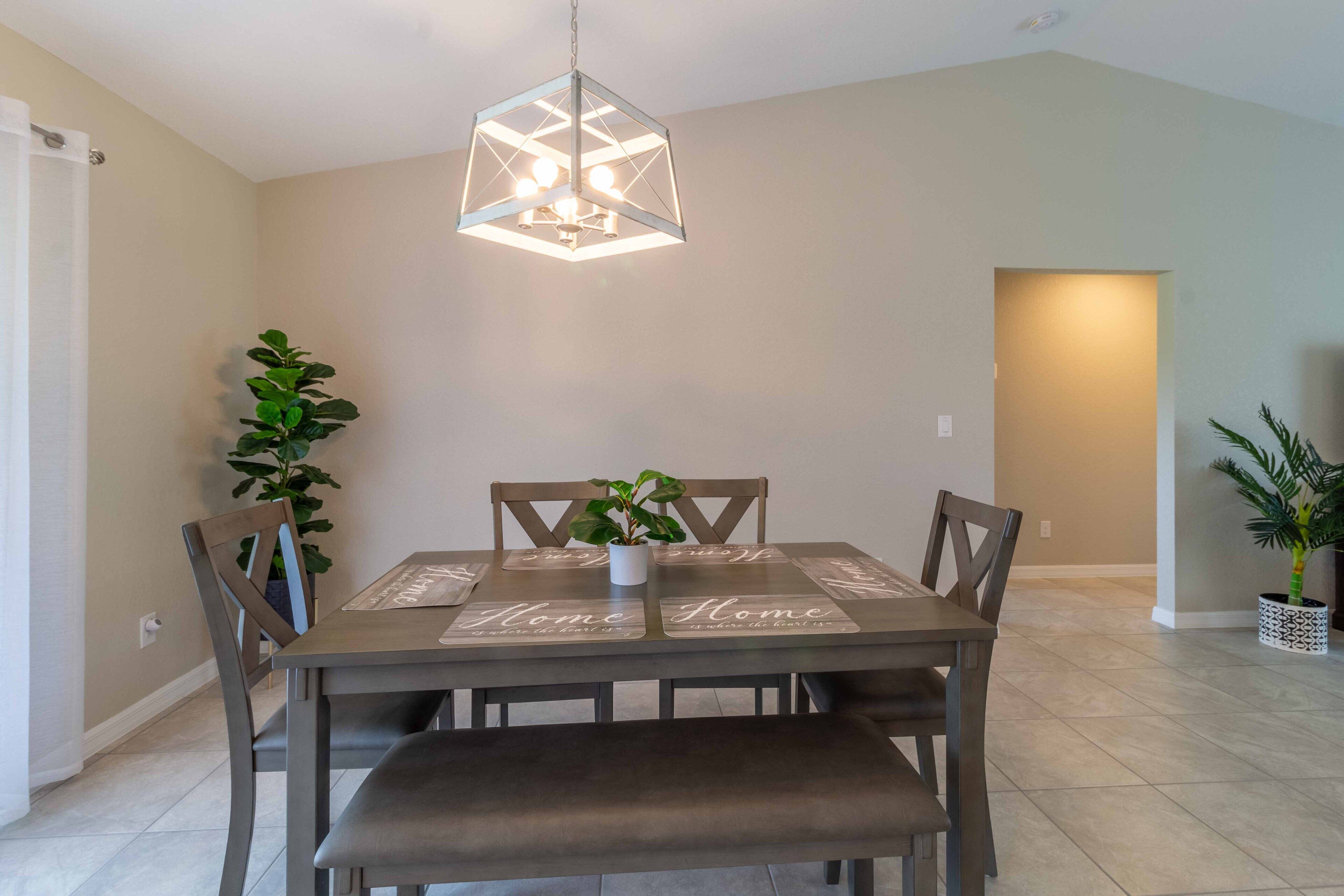 A dining area with a table set for four, a hanging light fixture, and two potted plants.