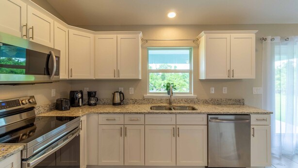 A modern kitchen with white cabinets, stainless steel appliances, a granite countertop, and a window providing natural light. - Brand new Private Home-Beach Nearby in SW Florida (Port Charlotte)
