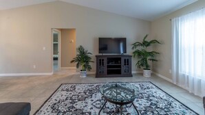 A spacious living room with a flat-screen TV on a dark wooden stand, a patterned rug, and two potted plants. - Brand new Private Home-Beach Nearby in SW Florida (Port Charlotte)