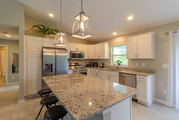 A modern kitchen with granite countertops, stainless steel appliances, and pendant lighting.