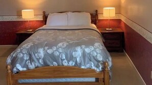A bed with a floral bedspread, two bedside lamps, and a wooden headboard in a room with red and beige walls. - Historical King George Inn 1 (Niagara-on-the-Lake)