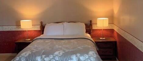 A bed with a floral bedspread, two bedside lamps, and a wooden headboard in a room with red and beige walls.