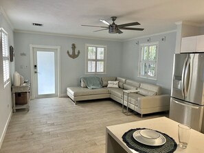 A modern living room with a sectional sofa, a dining table, and a kitchen area with a refrigerator. - New 2/1 Remodeled Cozy Home in Tavernier Key (Tavernier)