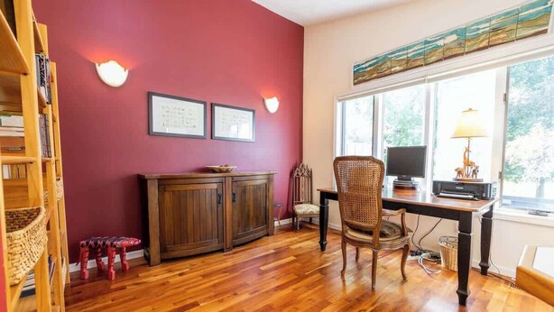 A room with a wooden floor, a desk with a computer, a chair, a bookshelf, and a window with a view of trees. - Crystal Lake Ridge, 30-day rental, community pool (Benzonia)