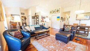 A spacious living room with a blue leather sofa, a matching ottoman, and a wooden coffee table. A patterned rug covers the floor, and the room has hardwood flooring. - Crystal Lake Ridge, 30-day rental, community pool (Benzonia)