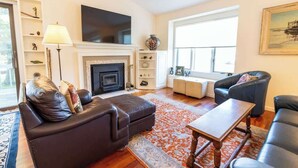 A living room with a fireplace, leather sofas, a coffee table, and a large window. - Crystal Lake Ridge, 30-day rental, community pool (Benzonia)