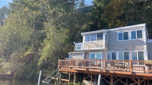 A two-story house with a wooden deck extending over water, surrounded by dense trees. - Lakefront & private beach  (Redmond)