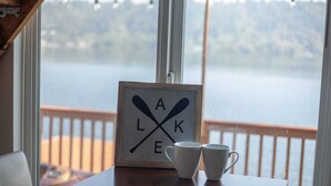 A framed sign with the letters "A L E K" crossed by two oars, two white cups on a table, and a view of a lake through a window. - Lakefront & private beach  (Redmond)