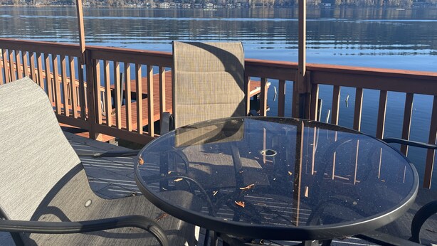 A deck with a glass table and chairs, overlooking a lake with a forested hillside in the background. - Lakefront & private beach  (Redmond)