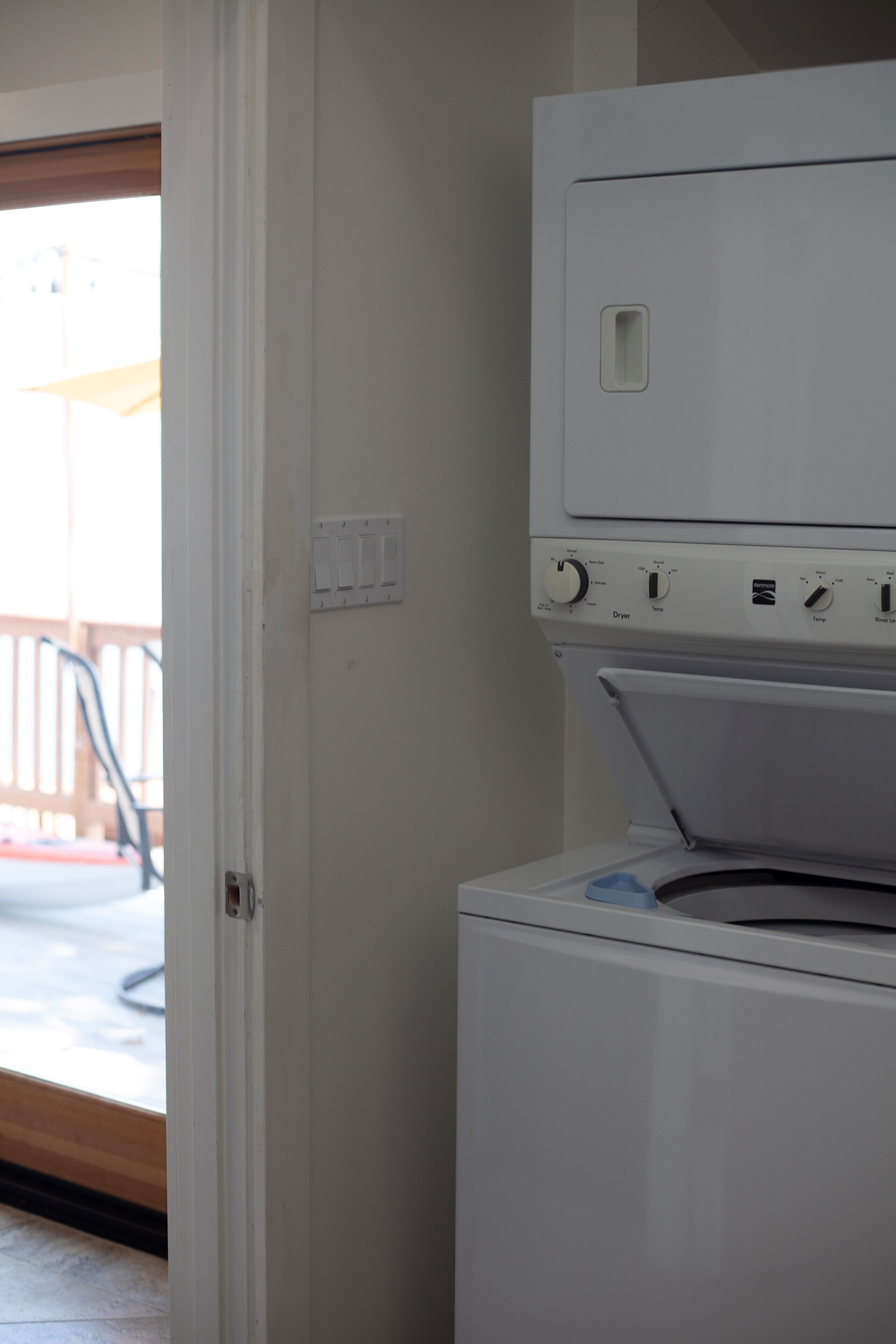 A laundry room with a front-loading washing machine and dryer, a door leading to an outdoor area, and a power outlet on the wall.