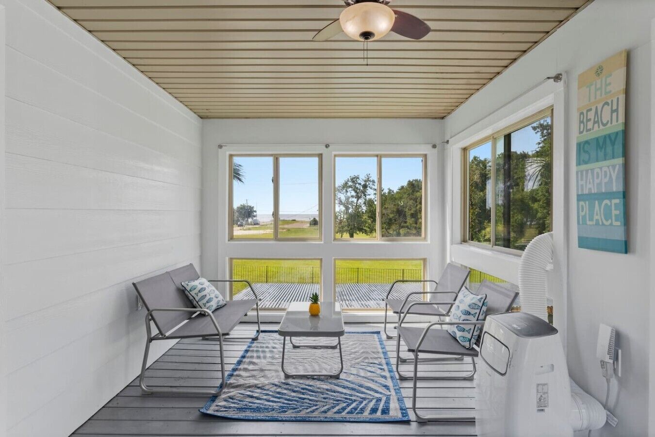 Eine überdachte Terrasse mit Deckenventilator, zwei Sitzbereiche mit Kissen, einem kleinen Tisch und Blick auf den Strand.