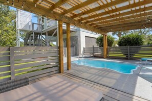 A covered outdoor swimming pool with wooden beams, a white fence with yellow accents, and a clear blue sky.