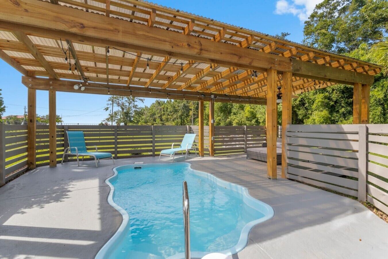 Une piscine extérieure couverte, dotée de chaises longues et d’une structure en forme de pergola.