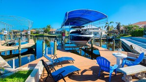 Een jachthaven met aangemeerde boten, een overdekte boot, lounge stoelen en een kleine tafel op een houten dek.