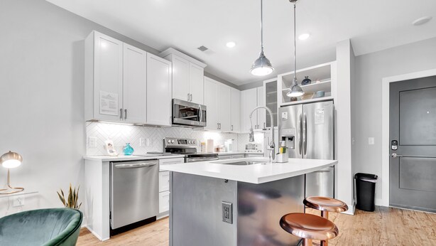 A modern kitchen with stainless steel appliances, a central island with stools, and a green chair. - Modern Luxury ☞ King Bed ☞ 1BR in Plaza Midwood (Charlotte)