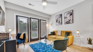 A modern living room with a yellow sofa, blue armchair, and a glass coffee table. - Modern Luxury ☞ King Bed ☞ 1BR in Plaza Midwood (Charlotte)