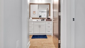 A hallway leading to a bathroom with white cabinets, a mirror, and a blue rug. - Modern Luxury ☞ King Bed ☞ 1BR in Plaza Midwood (Charlotte)