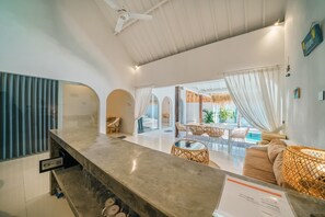 A modern hotel interior with a bar area, dining space, and a pool view. - Villa Santorini (Canggu)