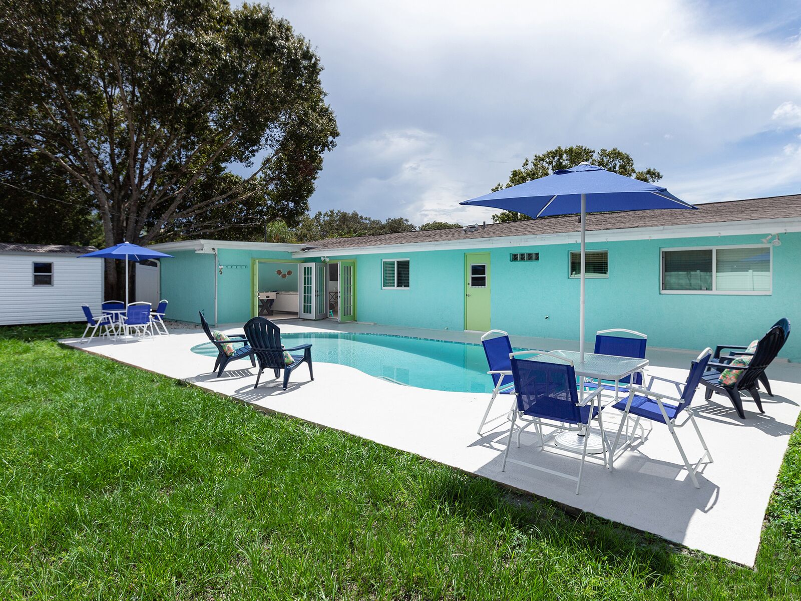 Un jardin avec une piscine, des chaises bleues et un espace patio couvert.