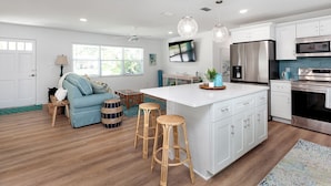 A modern kitchen with white cabinets, stainless steel appliances, and a central island with stools. - Designer Coastal Pool + Game Room home close to Siesta and downtown (Sarasota)