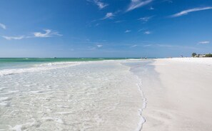 Una playa con agua cristalina, una orilla arenosa y algunas personas a lo lejos.