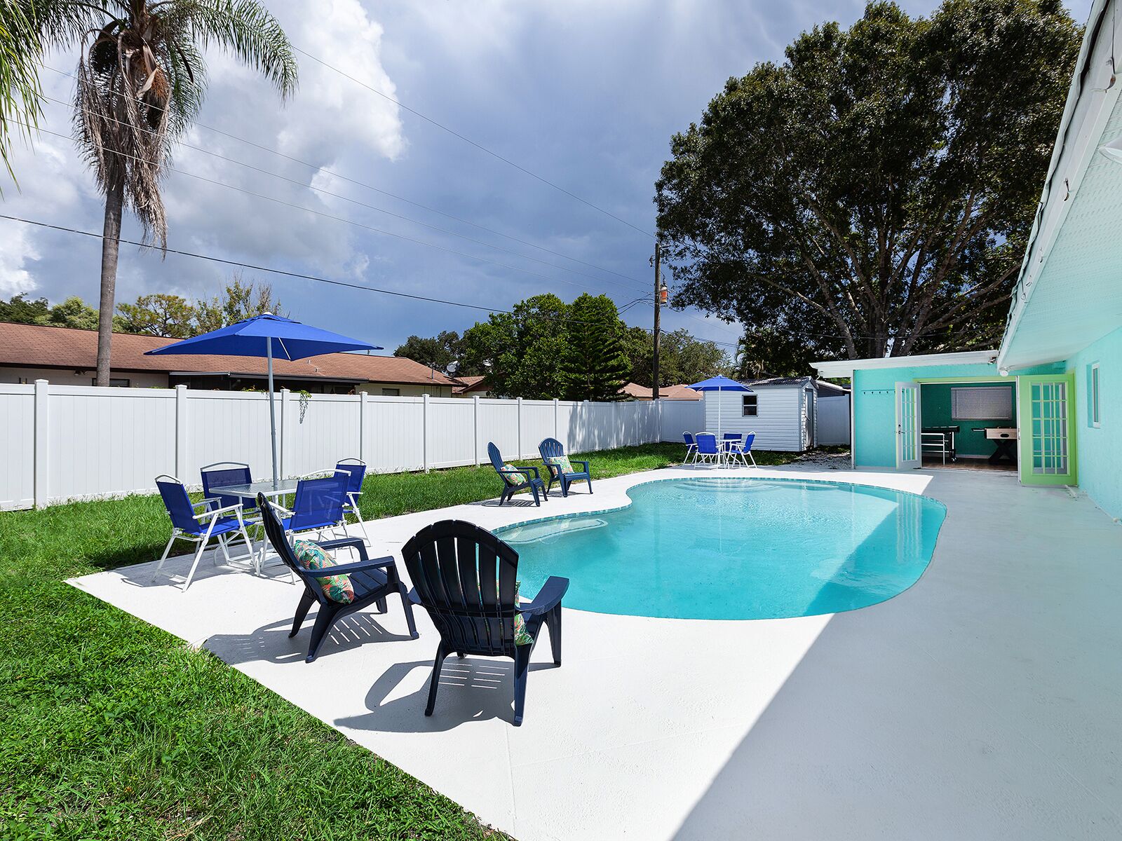 Patio con piscina, sillas azules y un cobertizo pequeño.