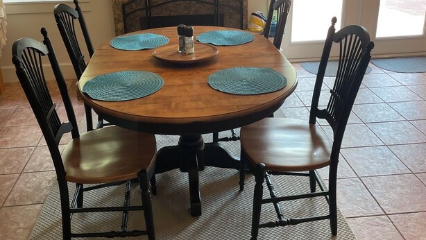 A dining area with a round wooden table, six black chairs, and a woven pendant light. - Canal front pool home to Dora Chain of Lakes (Tavares)