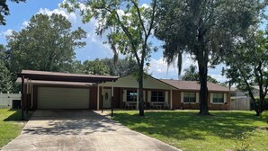A single-story house with a garage, a covered porch, and a front yard with trees and grass. - Canal front pool home to Dora Chain of Lakes (Tavares)
