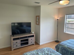 A bedroom with a TV on a wooden stand, a bedside table, a floor lamp, and a window with a view of a fence. - Canal front pool home to Dora Chain of Lakes (Tavares)