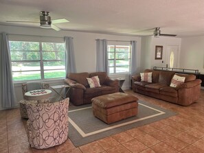 A living room with two brown leather sofas, a patterned ottoman, a glass coffee table, and a ceiling fan. - Canal front pool home to Dora Chain of Lakes (Tavares)