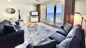Un soggiorno con divano, tavolino, televisione e un balcone vista oceano.