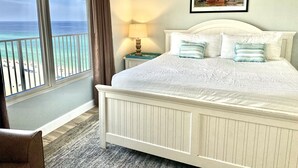 Una camera da letto con un letto grande, vista sulla spiaggia, un quadro appeso e un comodino con una lampada.